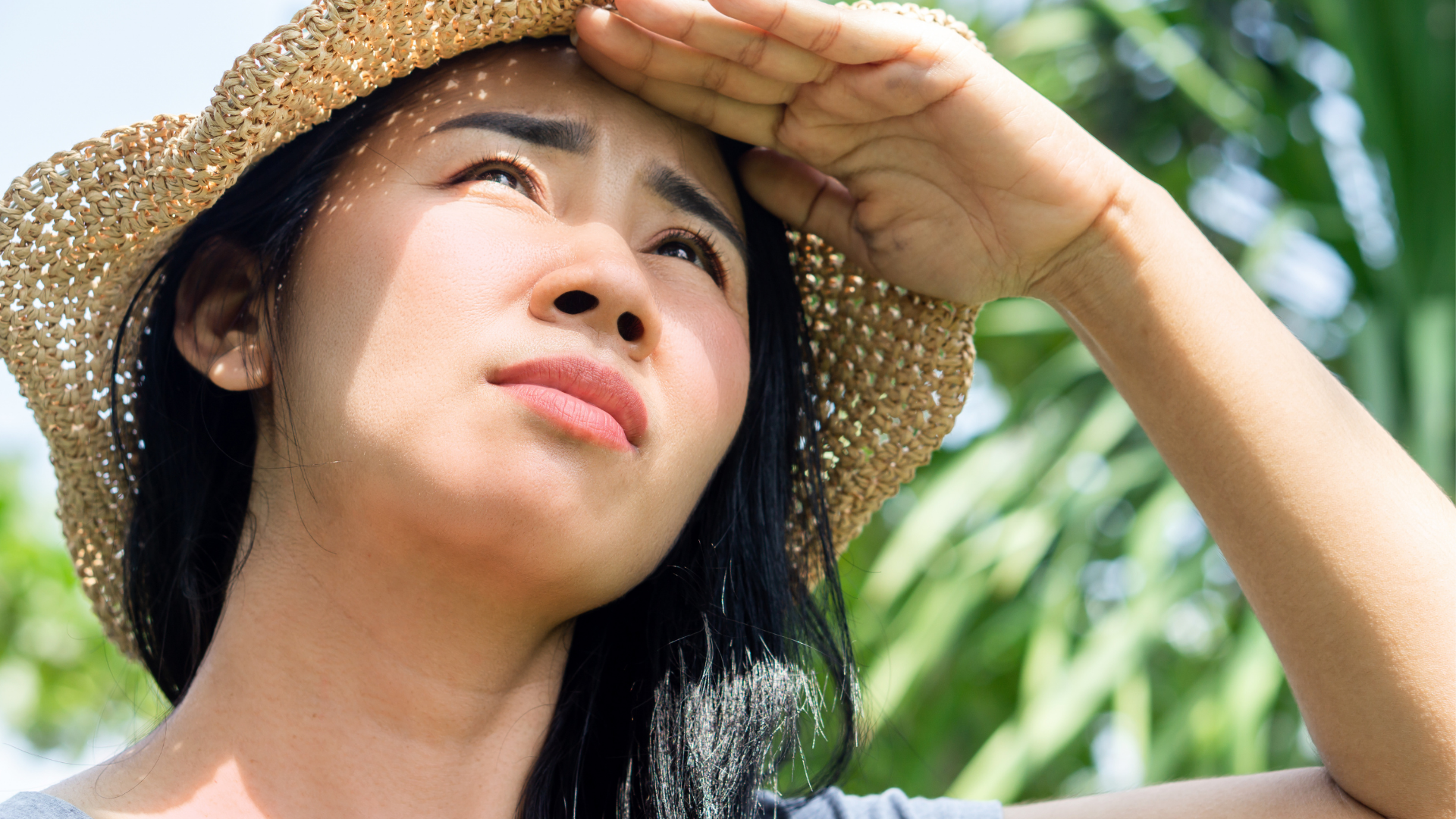 Young woman in a straw hat looking up into the summer sun, shielding her face